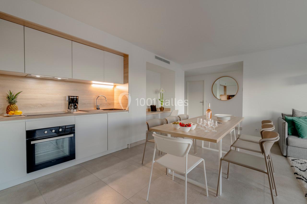 Cuisine moderne ouverte avec table à manger, chaises, canapé, et décoration minimaliste dans un espace lumineux.