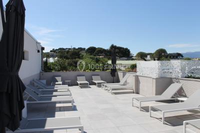 Terrasse extérieure éclairée la nuit avec des tables, des chaises longues et une vue sur une piscine illuminée.