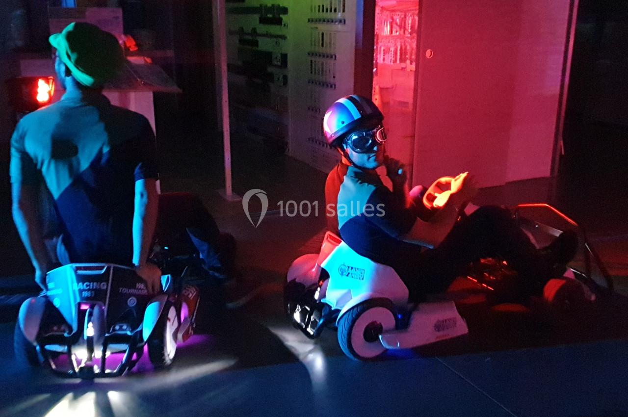 Deux personnes conduisent des karts électriques lumineux dans un environnement sombre avec des éclairages colorés.