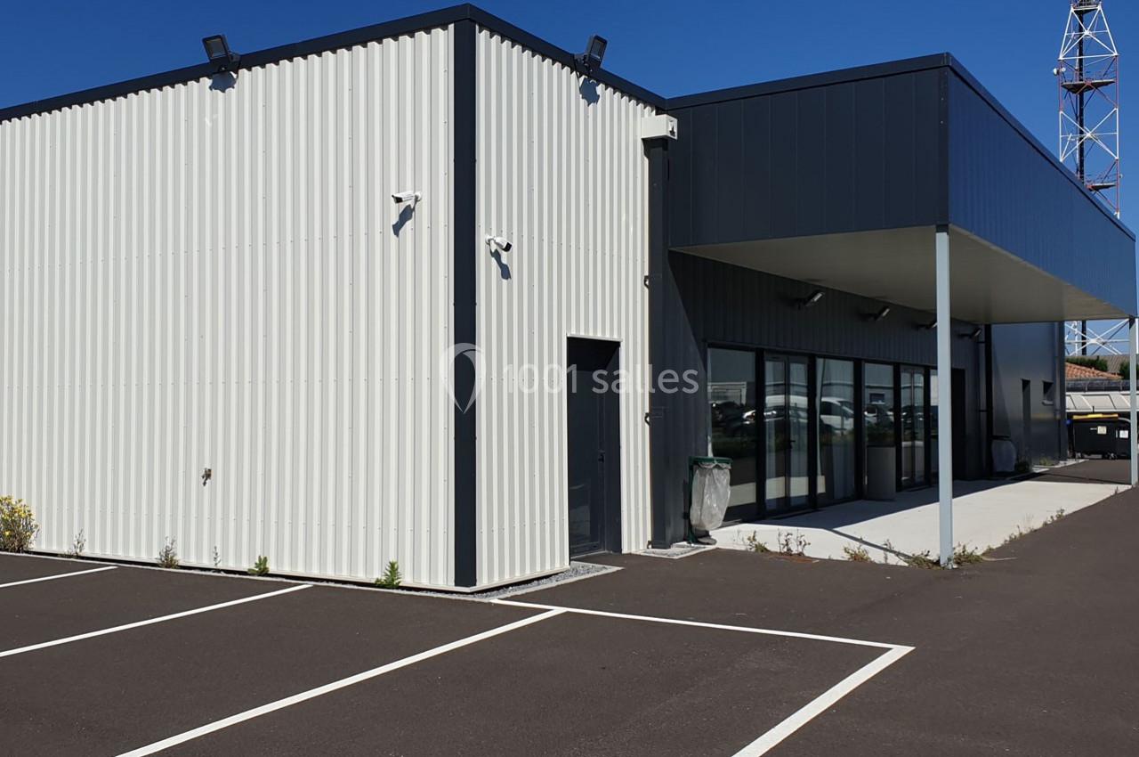 Bâtiment industriel moderne avec façade en métal, parking asphalté et antenne visible en arrière-plan.