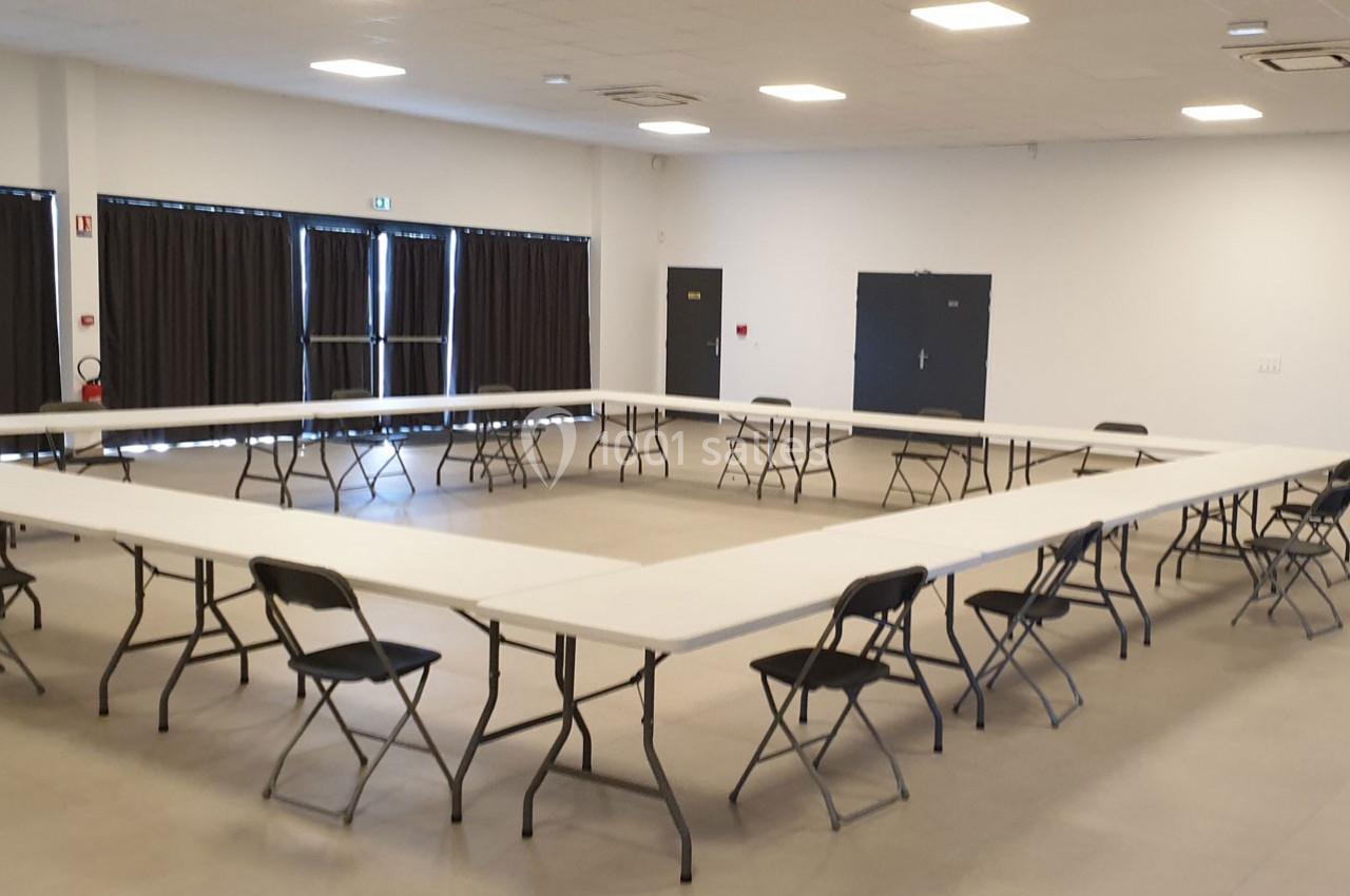 Salle lumineuse avec des tables disposées en U et des chaises noires, prête pour une réunion ou une formation.