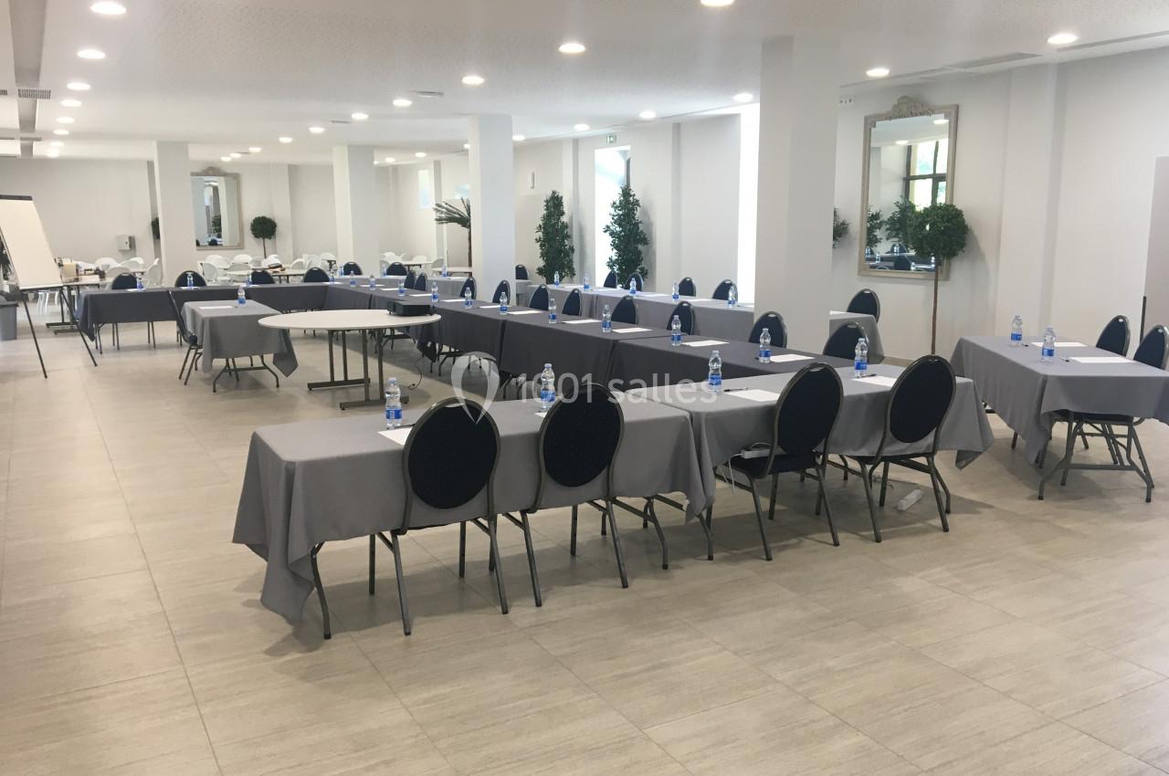 Salle de réunion lumineuse avec des tables disposées en U, chaises noires et bouteilles d'eau sur les tables.