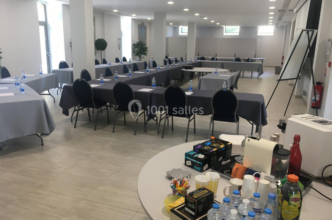Salle de réunion lumineuse avec tables disposées en U, chaises noires, et table de collation au premier plan.