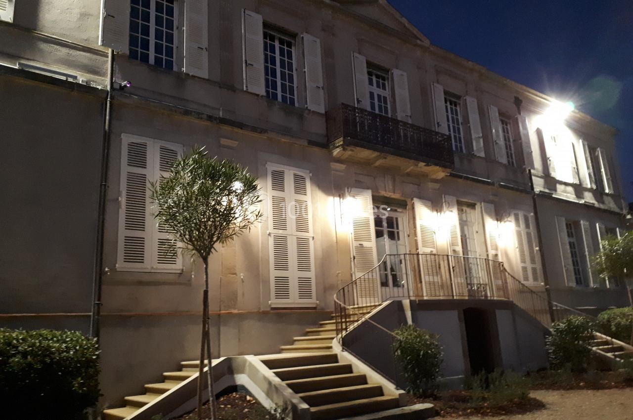 Façade d'un bâtiment ancien éclairé la nuit, avec des escaliers et des volets blancs.