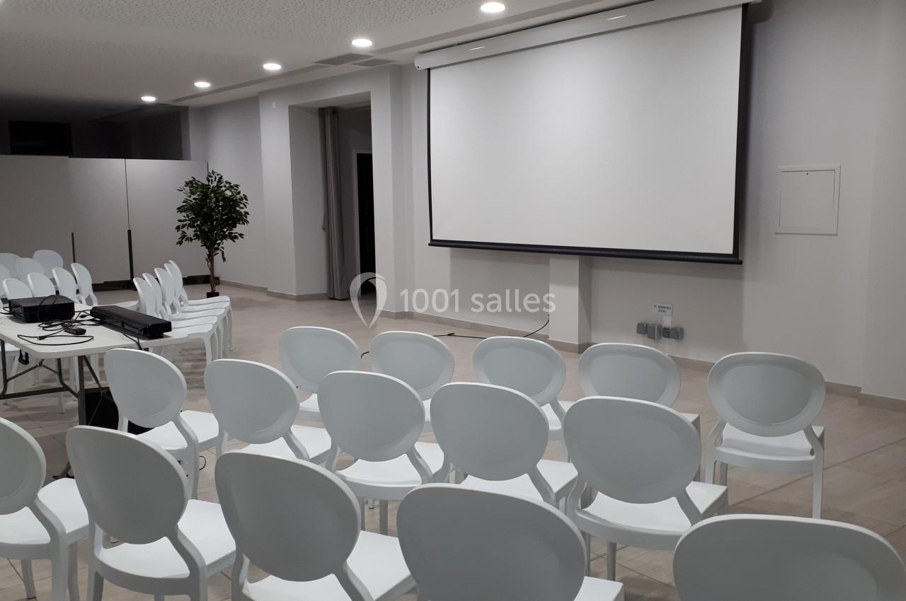 Salle de conférence avec des chaises blanches alignées, un projecteur et un écran de projection déployé.