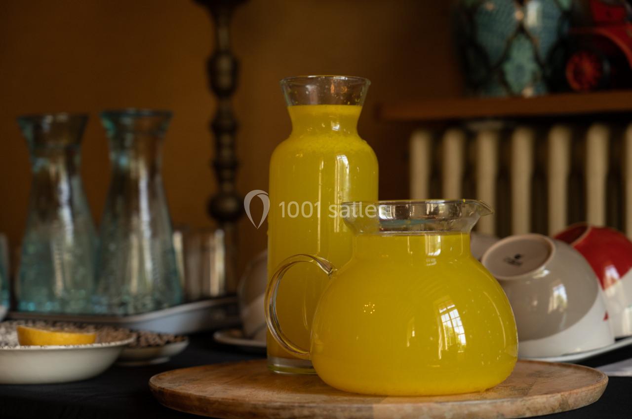 Carafes remplies de jus d'orange posées sur une table en bois, avec de la vaisselle en arrière-plan.