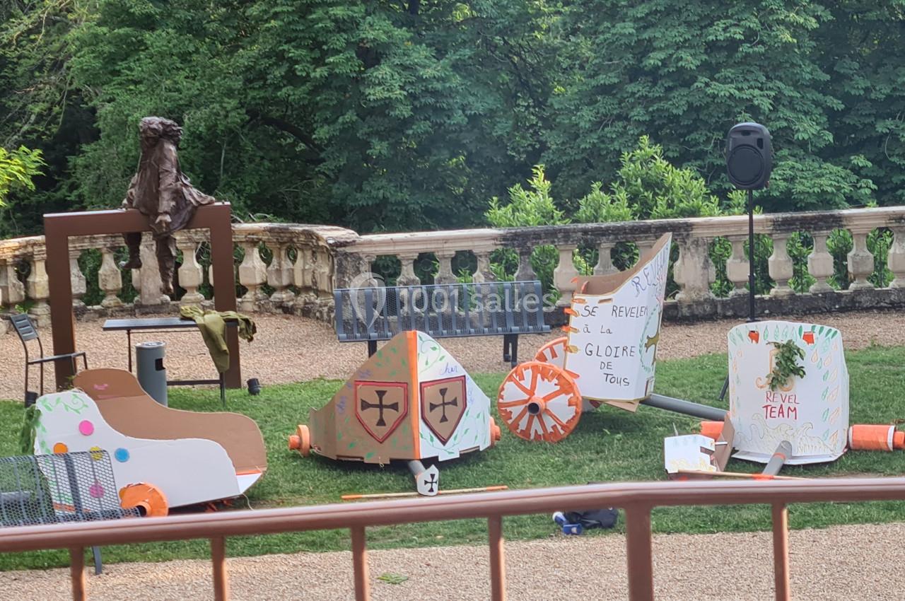 Des décors en carton colorés représentant des éléments médiévaux sont disposés sur une pelouse devant des arbres.