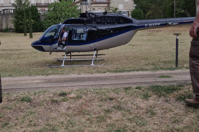 Un hélicoptère posé sur une pelouse, entouré d'arbres et de bâtiments en arrière-plan.