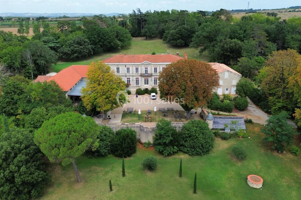 Vue aérienne d'un grand bâtiment ancien entouré de jardins verdoyants et d'arbres, dans un cadre rural.