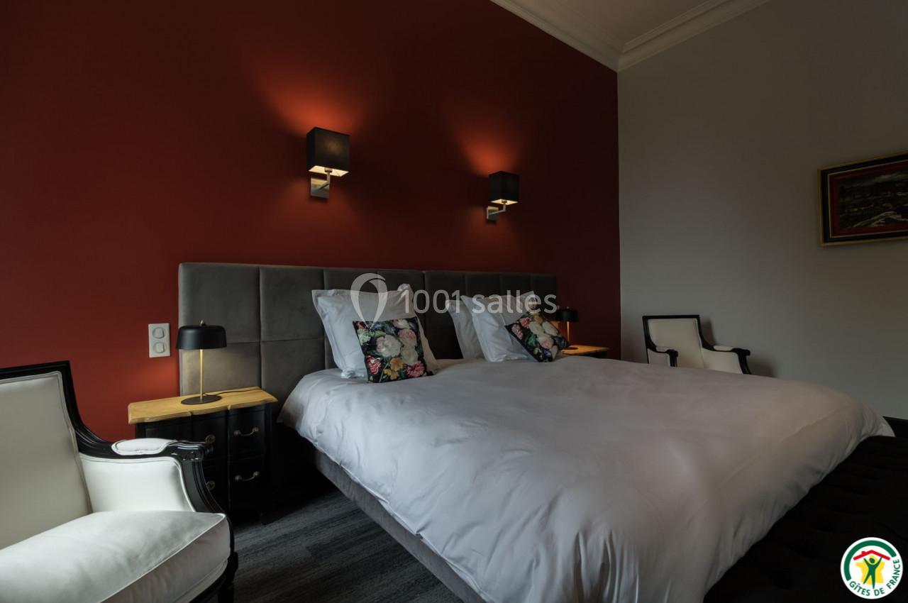 Lit double avec tête de lit capitonnée, deux lampes murales, coussins décoratifs et fauteuils dans une chambre élégante.