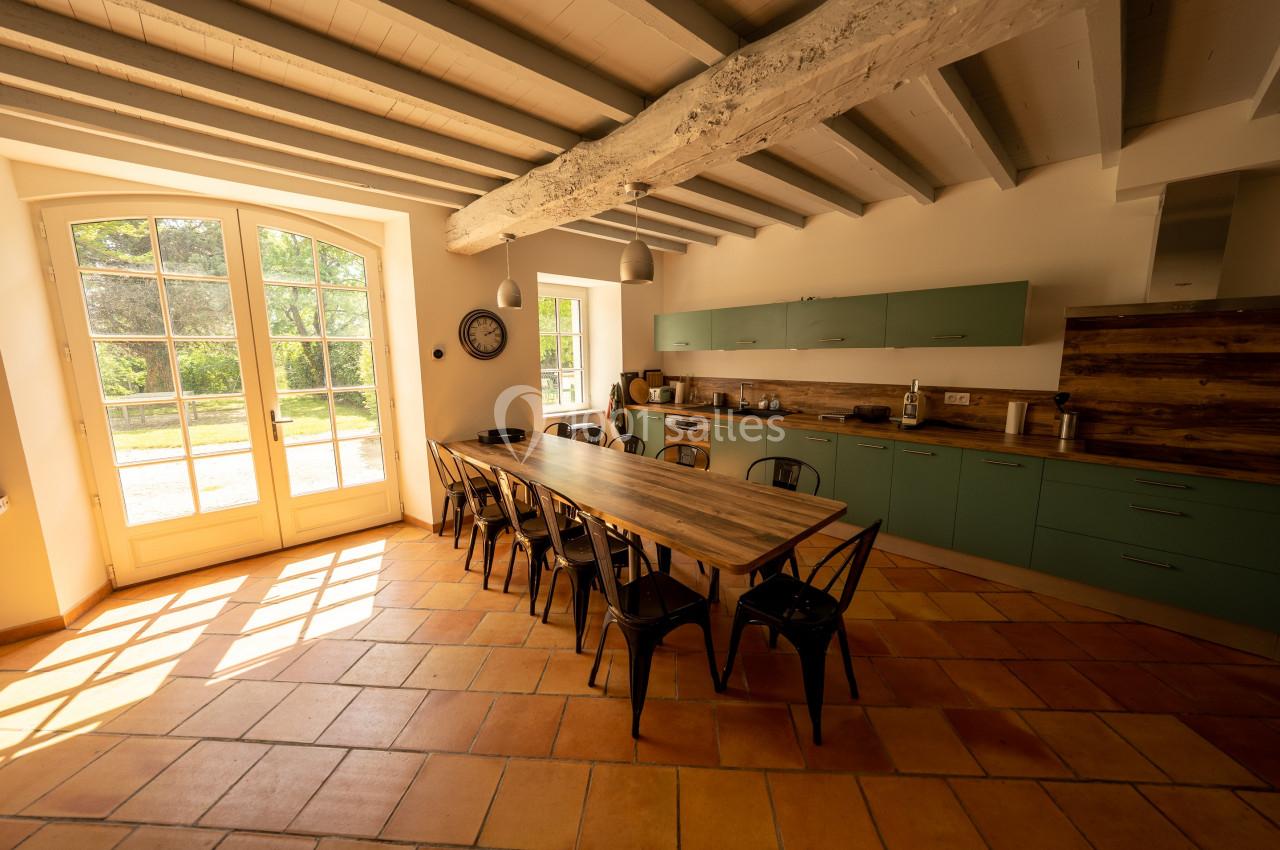 Cuisine lumineuse avec table en bois, chaises métalliques, poutres apparentes et vue sur un jardin par une grande baie…