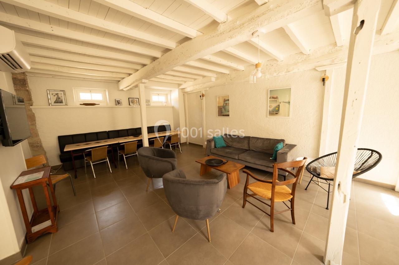 Salle de séjour lumineuse avec poutres apparentes, canapé, fauteuils, table à manger et décoration murale.
