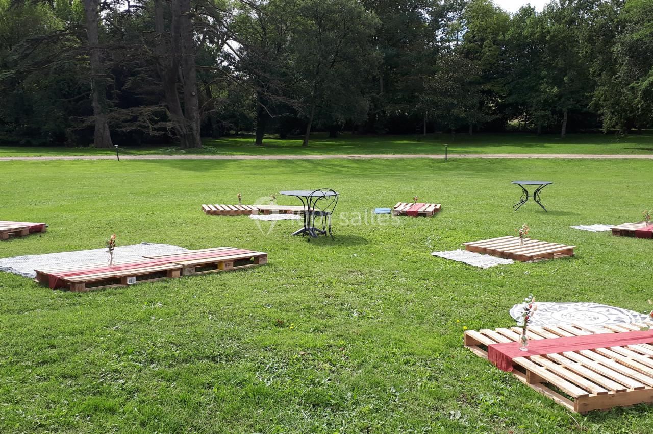 Palettes en bois aménagées en assises avec nappes et décorations sur une pelouse dans un parc verdoyant.