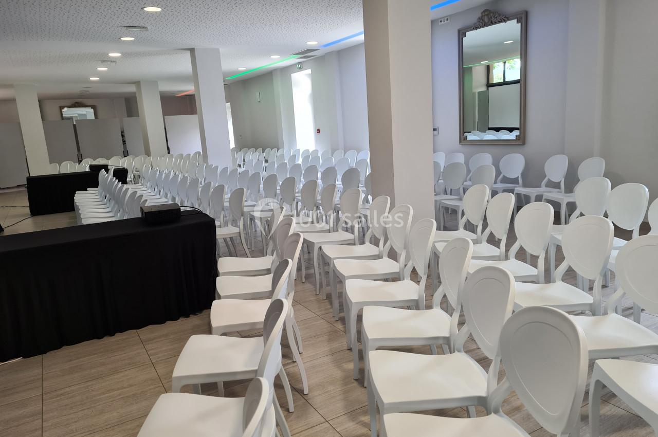 Salle de conférence lumineuse avec des rangées de chaises blanches alignées face à une table noire.