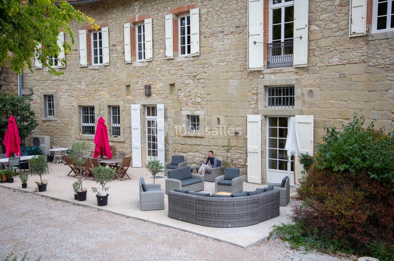 Cour d'une maison en pierre avec mobilier de jardin, parasols rouges et végétation environnante.