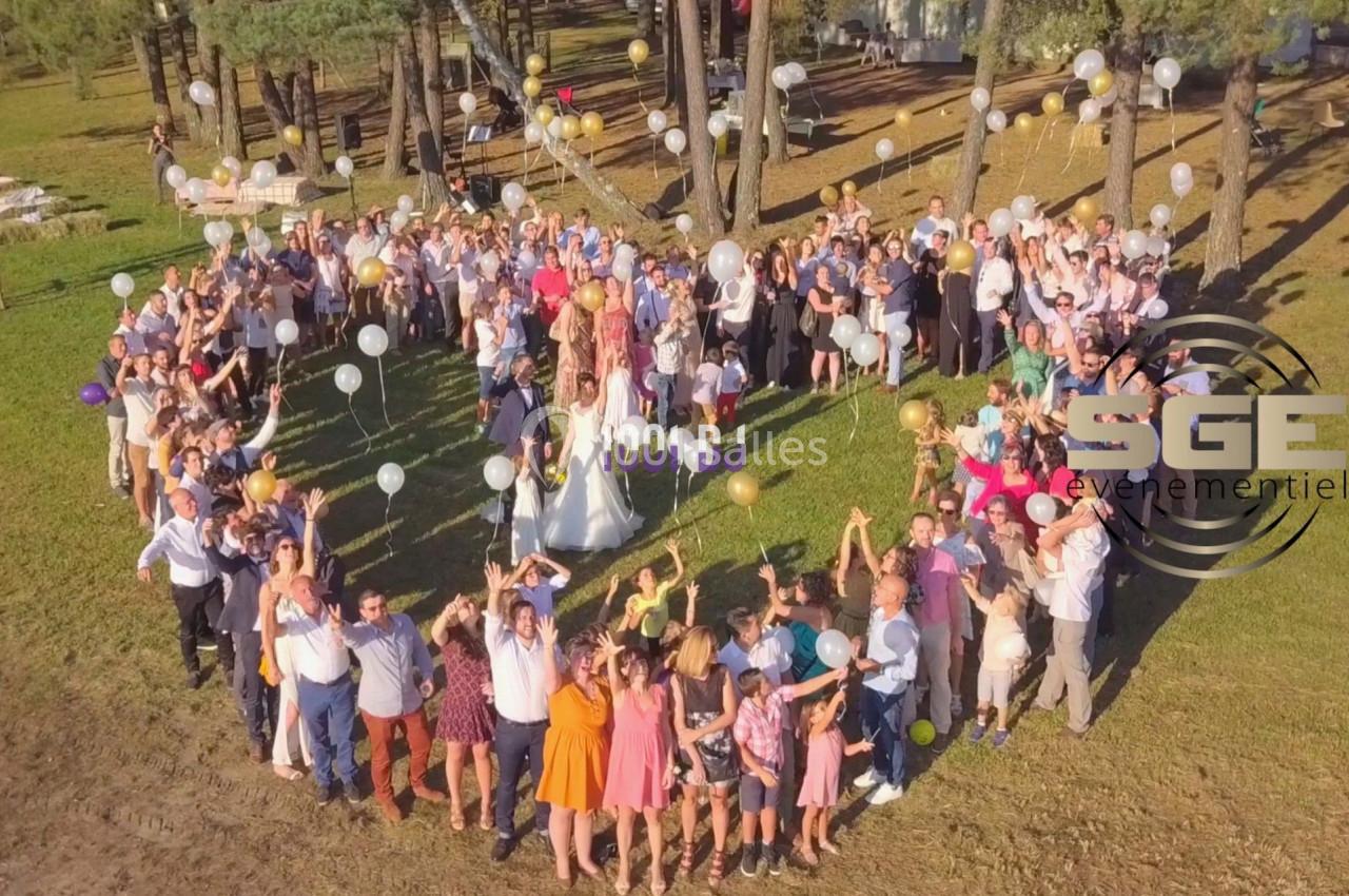 Groupe de personnes rassemblées en plein air, tenant des ballons, lors d'une célébration festive sous des arbres.