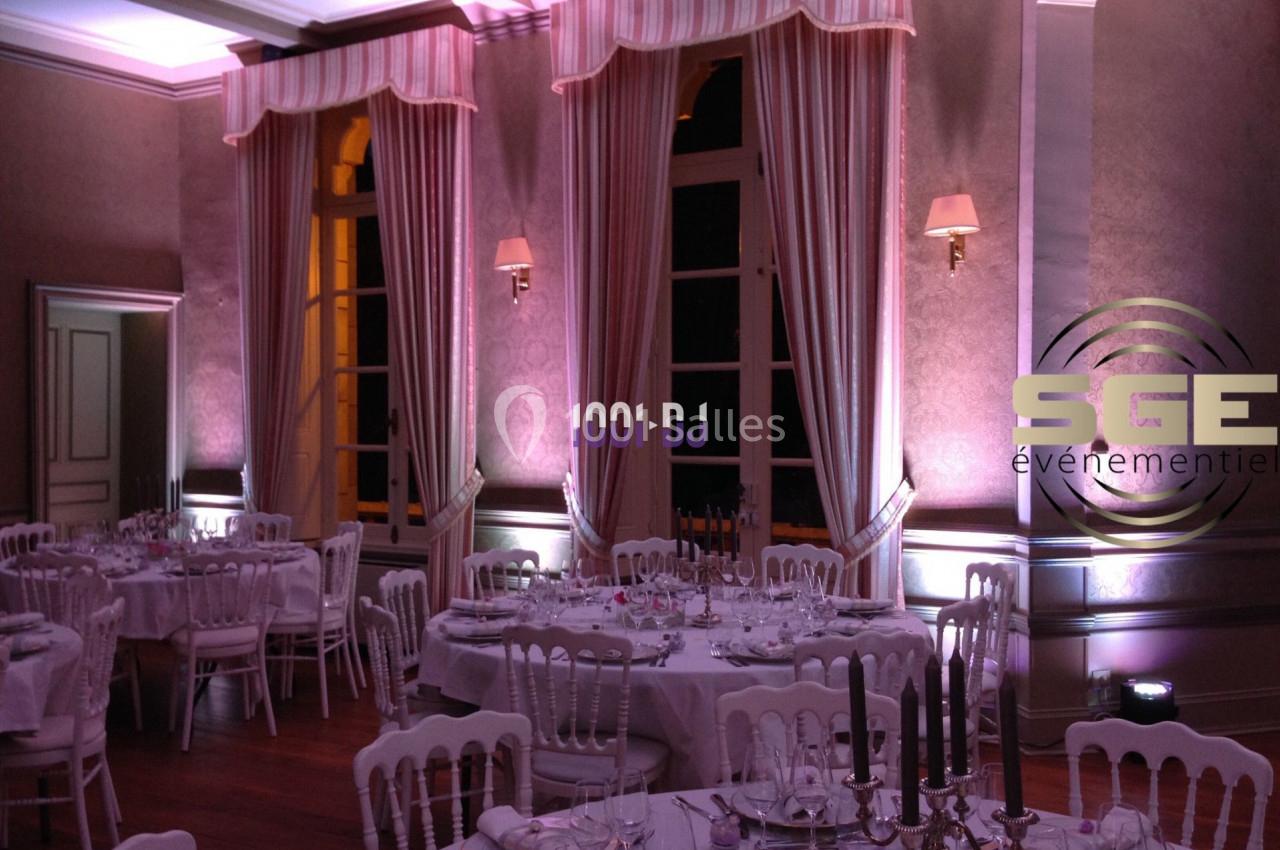 Salle de réception décorée avec des tables dressées, éclairage tamisé et rideaux encadrant de grandes fenêtres.