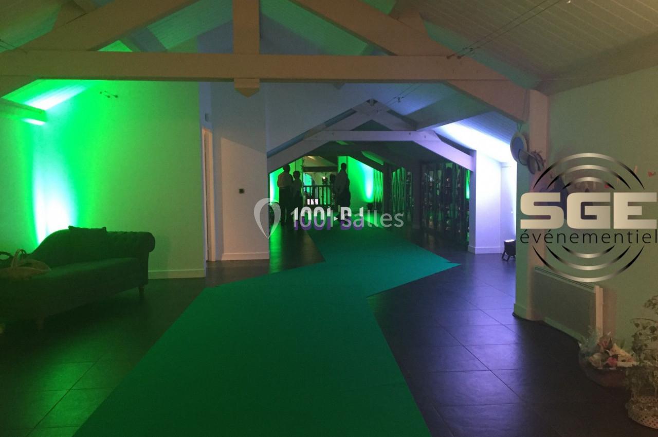 Salle de réception avec éclairage vert, tapis vert au sol et mobilier disposé le long des murs.