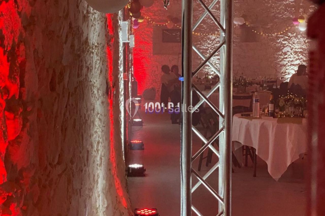 Salle en pierre éclairée de lumières rouges et blanches, avec des tables dressées et des équipements d'éclairage.