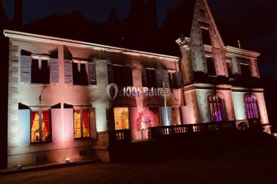 Façade en pierre éclairée par des lumières violettes, avec une porte voûtée et un sol en dalles.
