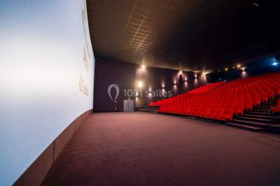 Façade vitrée d'un cinéma moderne sous un ciel bleu, avec trottoir et bâtiments en arrière-plan.