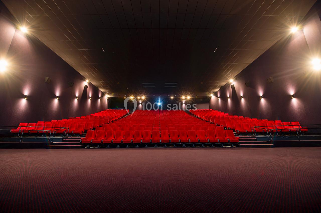 Salle de cinéma vide avec rangées de sièges rouges, éclairage tamisé et écran non visible à l'avant.