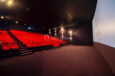 Façade vitrée d'un cinéma moderne sous un ciel bleu, avec trottoir et bâtiments en arrière-plan.