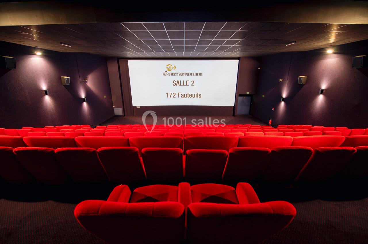 Salle de cinéma vide avec des fauteuils rouges, un écran affichant ’Salle 2, 172 fauteuils’ et un éclairage tamisé.