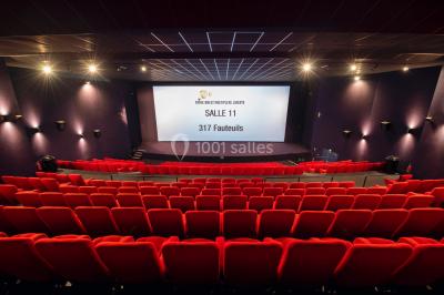 Façade vitrée d'un cinéma moderne sous un ciel bleu, avec trottoir et bâtiments en arrière-plan.