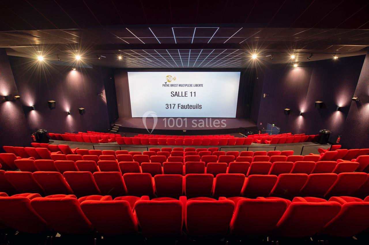 Salle de cinéma vide avec des rangées de fauteuils rouges, un écran géant et un éclairage tamisé.