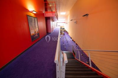 Façade vitrée d'un cinéma moderne sous un ciel bleu, avec trottoir et bâtiments en arrière-plan.