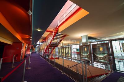 Façade vitrée d'un cinéma moderne sous un ciel bleu, avec trottoir et bâtiments en arrière-plan.