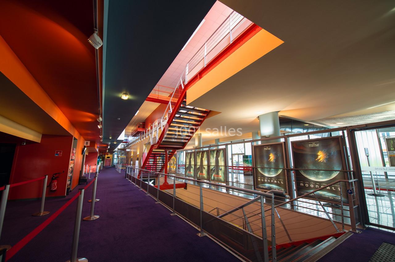 Escalier moderne dans un hall spacieux avec moquette violette, affiches de films et lumière naturelle.