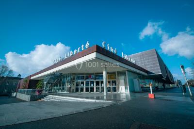 Façade vitrée d'un cinéma moderne sous un ciel bleu, avec trottoir et bâtiments en arrière-plan.