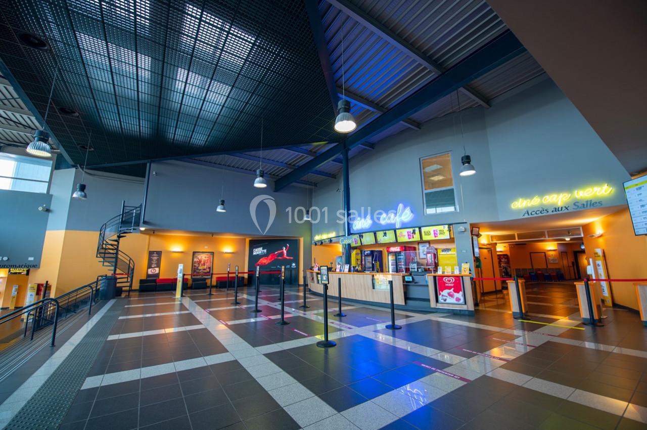 Hall d'entrée spacieux avec comptoir de café, affiches murales et accès aux salles de cinéma.