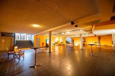 Couloir d'un cinéma avec moquette beige, murs orange, portes numérotées et éclairage chaleureux.