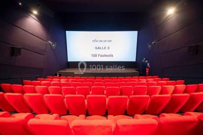 Couloir d'un cinéma avec moquette beige, murs orange, portes numérotées et éclairage chaleureux.