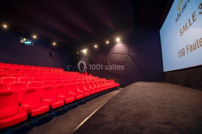 Couloir d'un cinéma avec moquette beige, murs orange, portes numérotées et éclairage chaleureux.