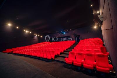 Couloir d'un cinéma avec moquette beige, murs orange, portes numérotées et éclairage chaleureux.