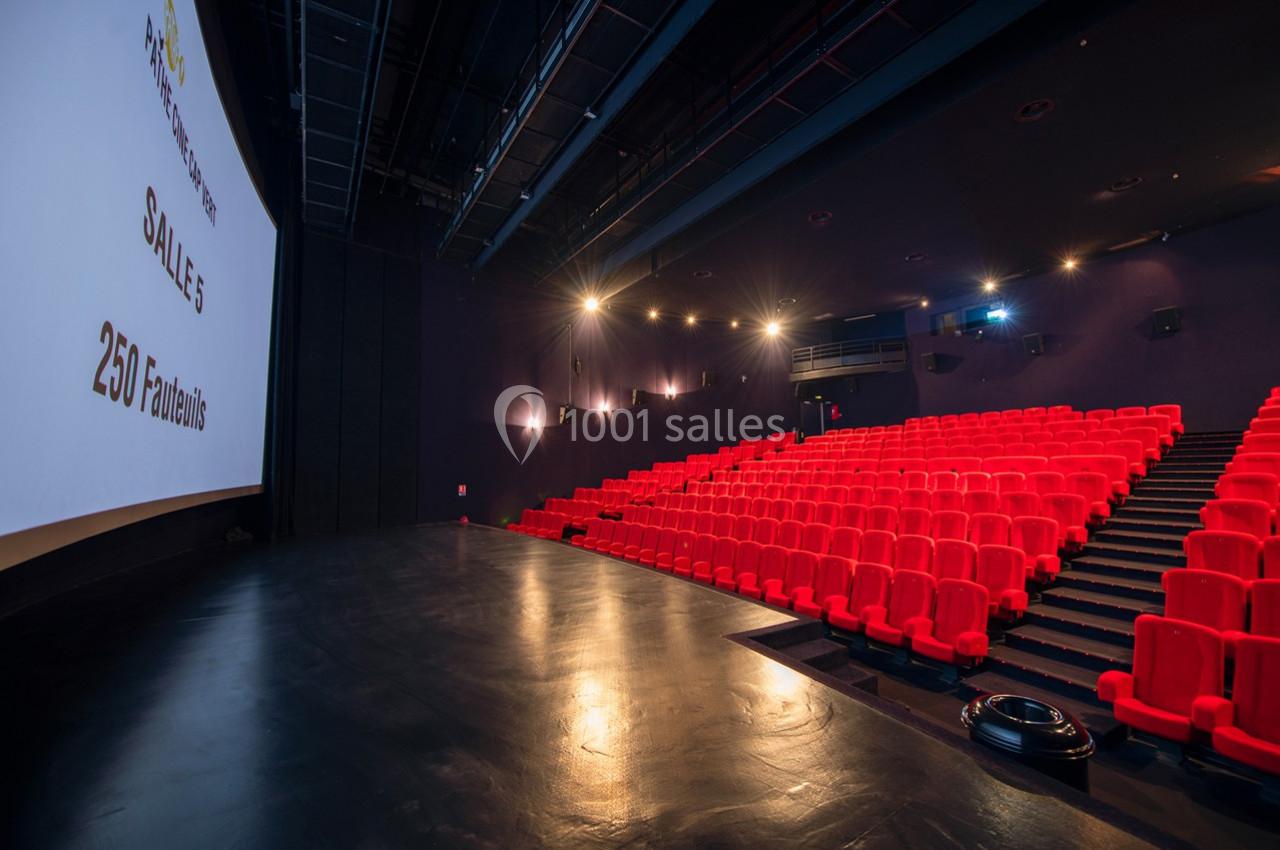 Salle de cinéma vide avec des rangées de sièges rouges, un écran blanc affichant ’Salle 5 - 250 fauteuils’.