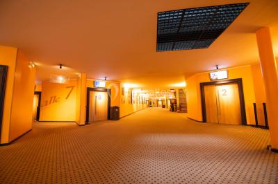 Couloir d'un cinéma avec moquette beige, murs orange, portes numérotées et éclairage chaleureux.