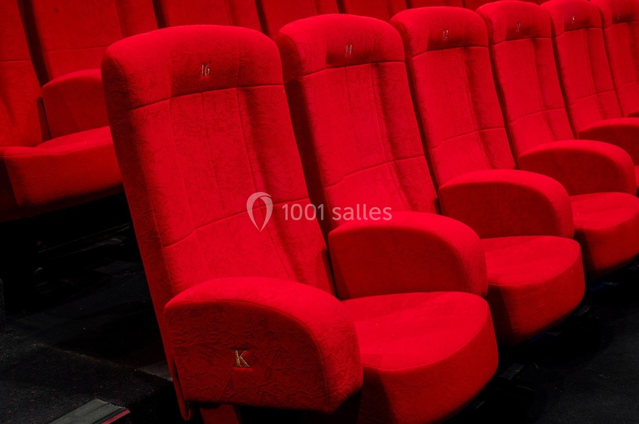 Rangée de fauteuils de cinéma rouges alignés dans une salle sombre.