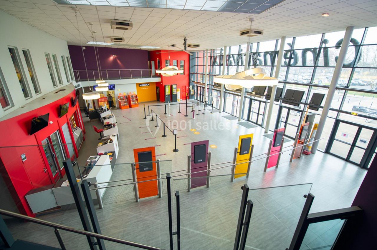 Hall d'entrée spacieux avec guichets, bornes automatiques, et file d'attente délimitée par des poteaux.