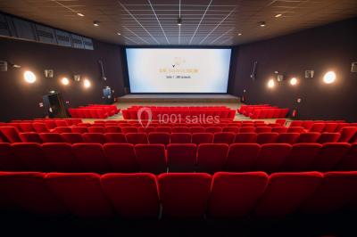 Salle de cinéma vide avec des rangées de sièges rouges et un grand écran allumé affichant un logo et du texte.