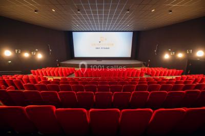 Salle de cinéma vide avec des rangées de sièges rouges et un grand écran allumé affichant un logo et du texte.