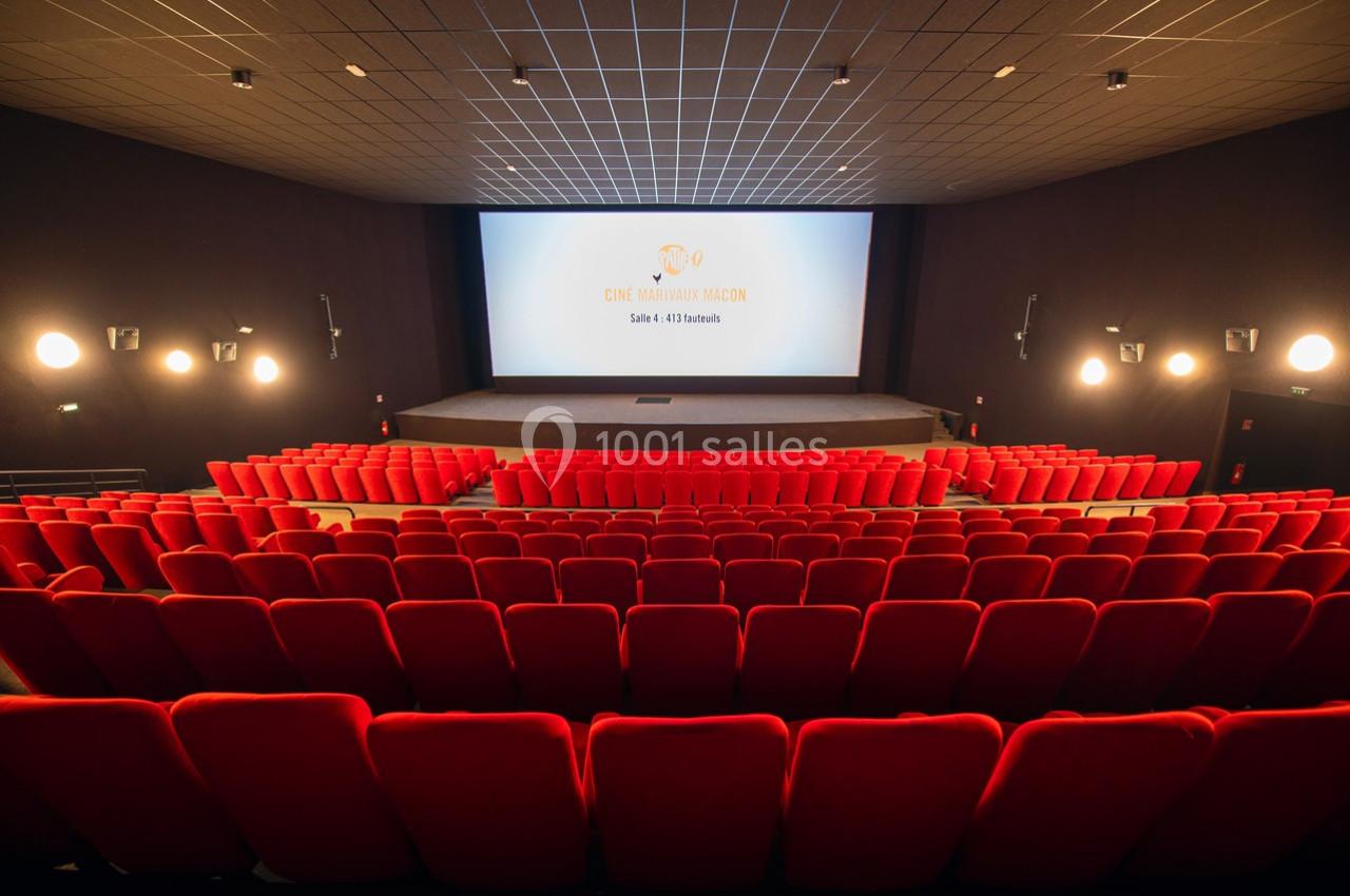 Salle de cinéma vide avec rangées de fauteuils rouges et écran blanc éclairé au fond.