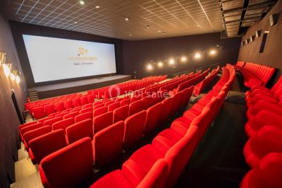 Salle de cinéma vide avec des rangées de sièges rouges et un grand écran allumé affichant un logo et du texte.