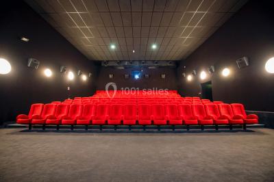 Salle de cinéma vide avec des rangées de sièges rouges et un grand écran allumé affichant un logo et du texte.