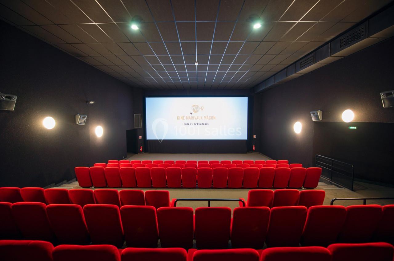 Salle de cinéma vide avec des rangées de fauteuils rouges et un écran blanc allumé au fond.