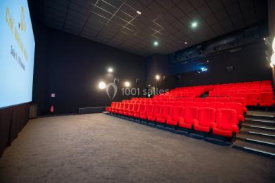 Salle de cinéma vide avec des rangées de sièges rouges et un grand écran allumé affichant un logo et du texte.